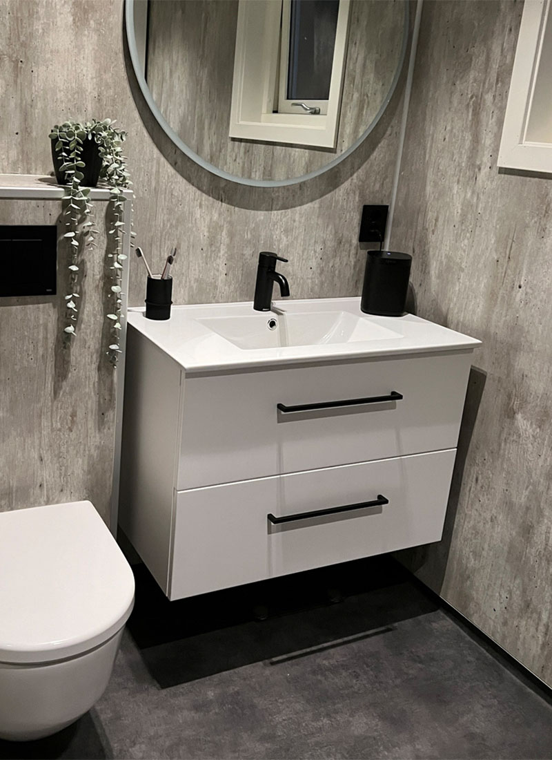 Fibo baderomsplater i cracked cement, hvitt baderomsmøbel med sorte detaljer og Vikingbad Oda rundt speil