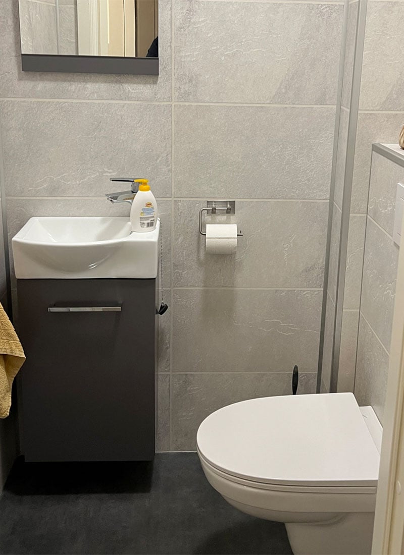 Lite toalettrom ved siden av hovedbad med veggskål og kompakt møbel
